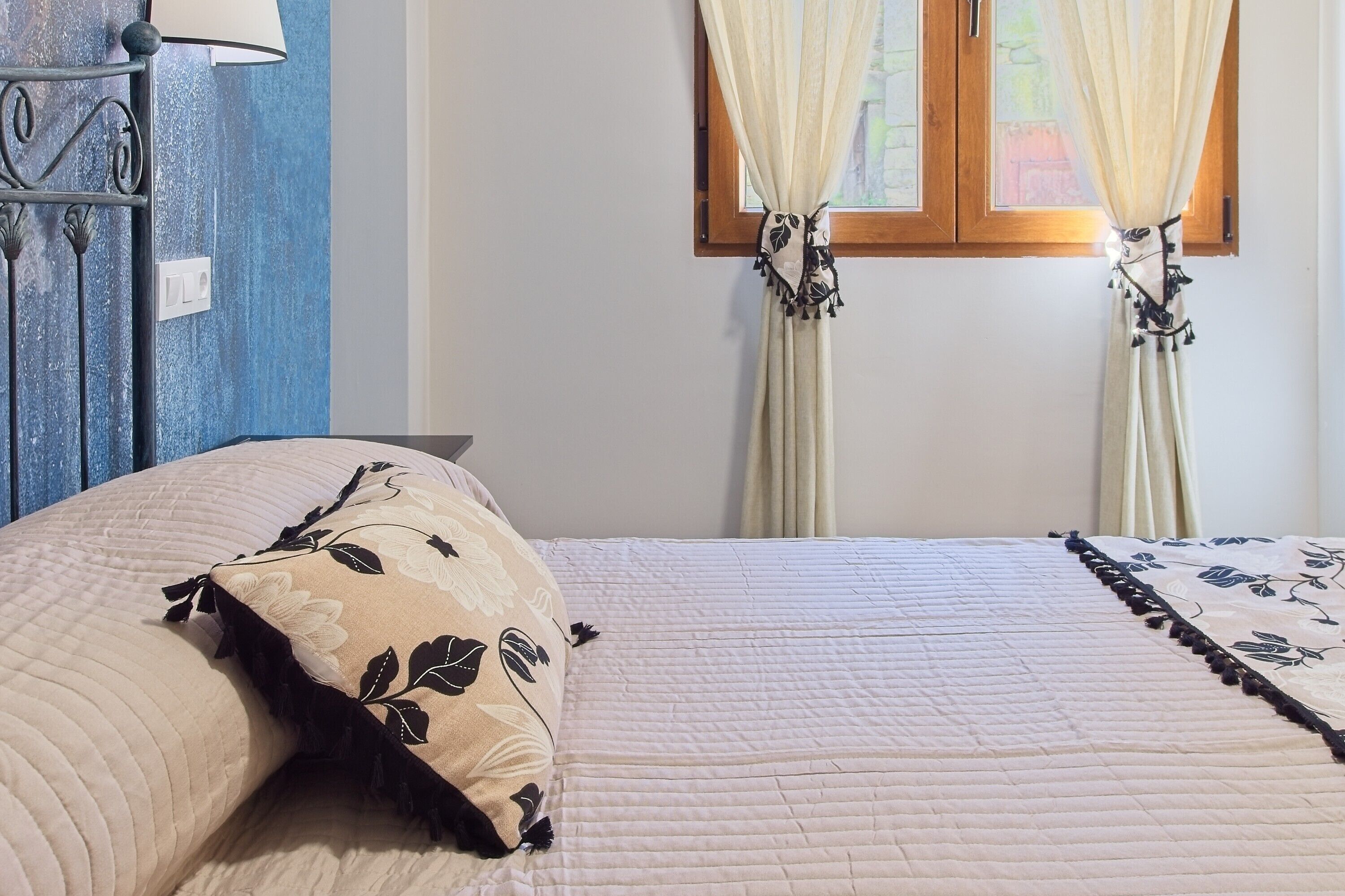 A bed with a floral pillow, a bedside table, and a window with curtains.