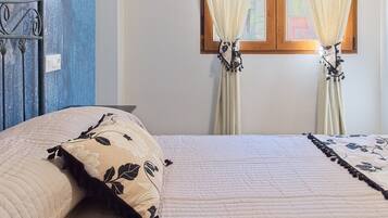 A bed with a floral pillow, a bedside table, and a window with curtains.