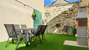 An outdoor patio with a stone wall, a grill, and a table with chairs. - Holiday Home 'Lago De Sanabria' with Mountain View, Private Garden and Balcony (Coso)