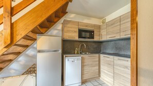A compact kitchen with a built-in microwave, dishwasher, and a wooden staircase. - Apartment 'Granges 35' with Mountain View and Balcony (Villard-Reculas)