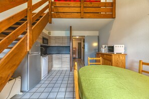 A room with a bed, wooden staircase, kitchenette, and a view into the hallway.