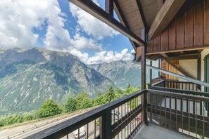 Un balcón con vista a la montaña, vigas de madera y barandilla de metal.