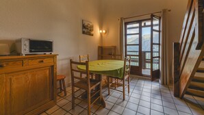 A kitchen with a dining table, chairs, a wooden cabinet, a microwave, and a window with a view of mountains. - Apartment 'Granges 35' with Mountain View and Balcony (Villard-Reculas)