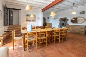 A dining area with a large wooden table and chairs, a staircase, and a kitchen area with wooden cabinets and a round mirror. - Cottage 'Can Ribes' with Outdoor Pool, Garden and Terrace (Camós)