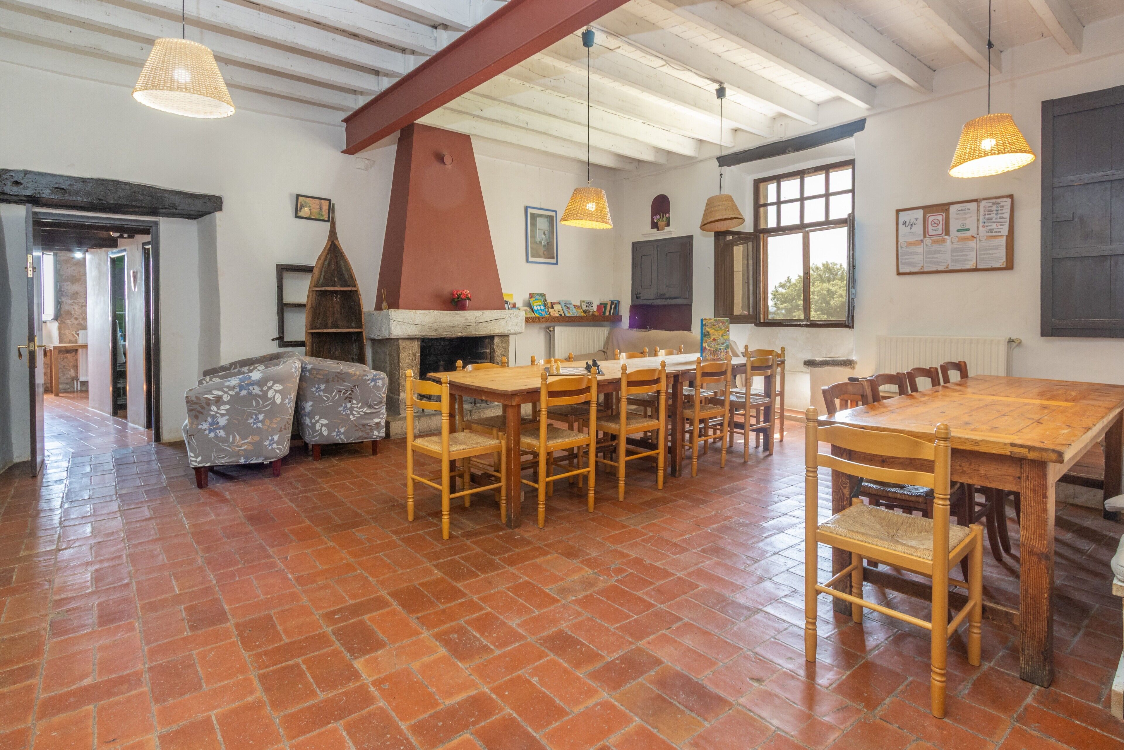 Un vaste espace dédié à la salle à manger, avec une grande table et des chaises en bois, une cheminée et des luminaires suspendus.
