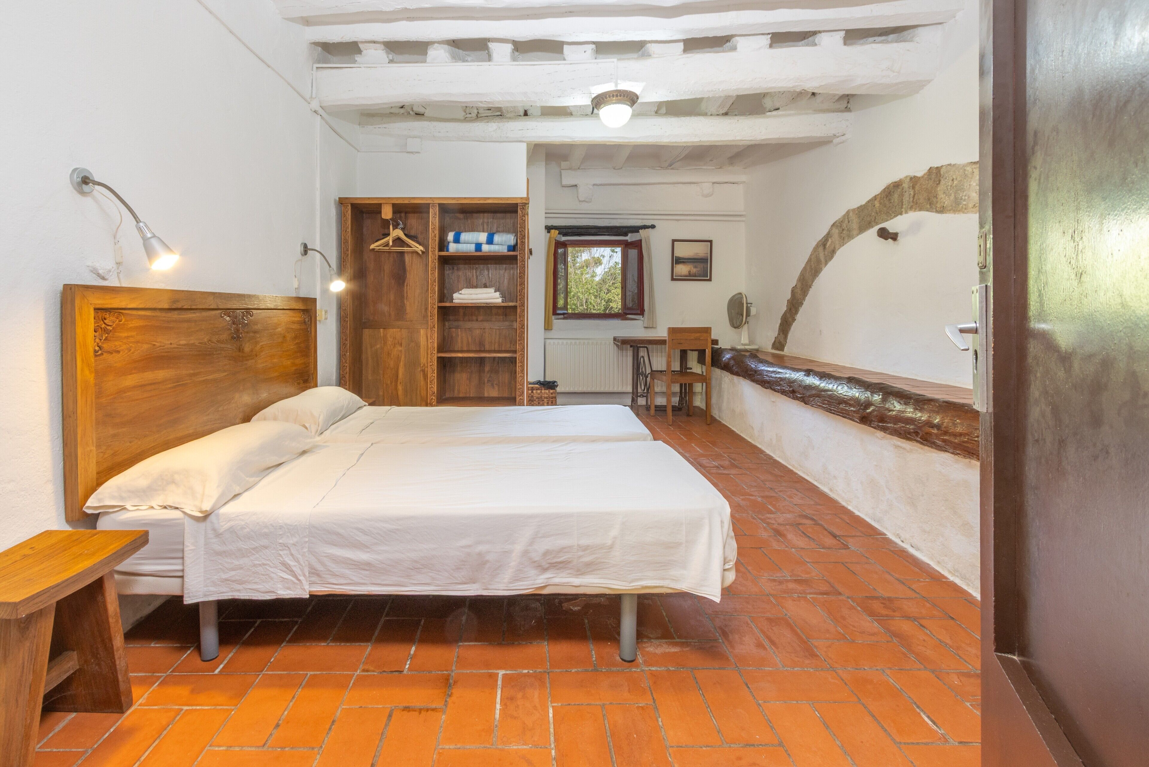 A room with a bed, a wooden wardrobe, a small table, and a window with a view.