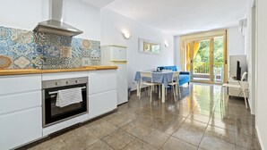 A kitchen with a tiled backsplash, a stove, a sink, and a dining area with chairs and a table.