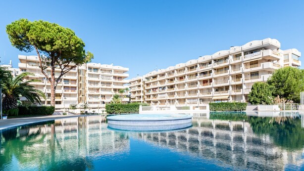 A hotel with a swimming pool, multiple balconies, and a large tree in the foreground.