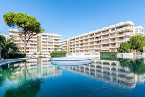 Un hotel amb piscina, diversos balcons i un arbre gran al primer pla.