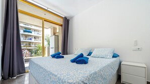 A bedroom with a bed, a nightstand, a window with curtains, and a view of a building outside.