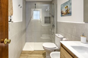 Ein Badezimmer mit Dusche, Toilette, Waschbecken und einem kleinen Fenster.
