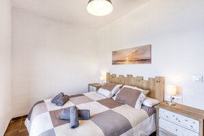 A bedroom with a checkered bedspread, two bedside tables with lamps, a painting on the wall, and a wooden headboard.