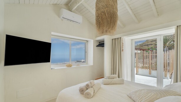 A bedroom with a bed, a TV mounted on the wall, a window with a view, and a ceiling fan. - Holiday Home 'Xuixo In Tenerife South' with Sea View, Wi-Fi and Air Conditioning (Guía de Isora)