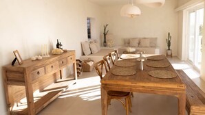 A spacious living area with a wooden dining table, a sofa, and a large window. - Holiday Home 'Xuixo In Tenerife South' with Sea View, Wi-Fi and Air Conditioning (Guía de Isora)