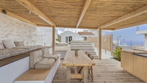 An outdoor patio with a wooden table and benches, a white wall, and a view of a house in the background. - Holiday Home 'Xuixo In Tenerife South' with Sea View, Wi-Fi and Air Conditioning (Guía de Isora)