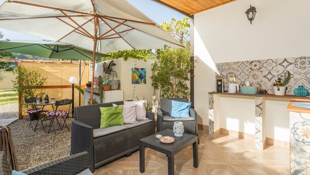 An outdoor patio area with wicker furniture, a table with decorative items, and a tiled backsplash in the background.