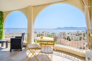 Un balcon avec une table ronde et deux chaises, une vue sur le paysage urbain et un ciel dégagé.