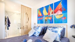 A hotel room with a bed, a shower, and a painting of sailboats.