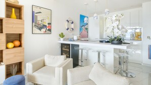 A modern kitchen with a white countertop, bar stools, and a potted plant.
