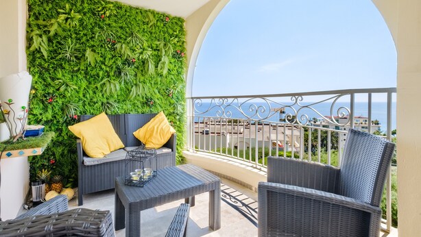 A balcony with wicker furniture, a green wall, and a view of the sea.