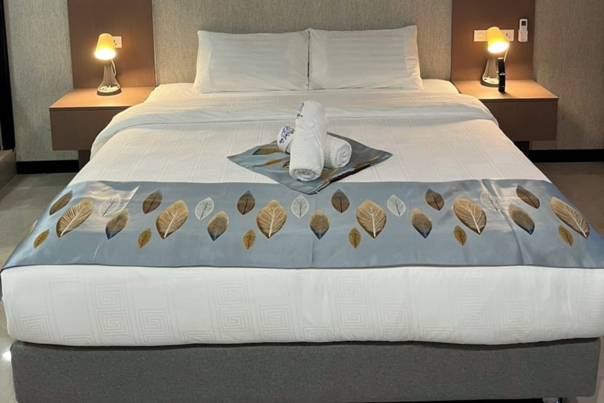 A modern hotel room with a large bed, two bedside tables with lamps, and a headboard with vertical panels.
