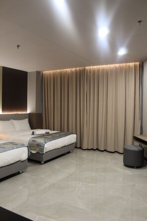 Une chambre d’hôtel moderne avec deux lits, une grande fenêtre avec des rideaux, un téléviseur à écran plat et un petit pouf.