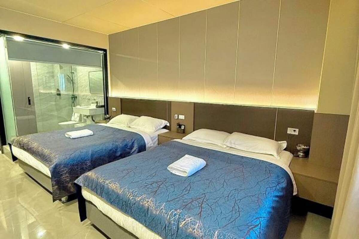 A hotel room with two beds, a glass partition, and a modern design.