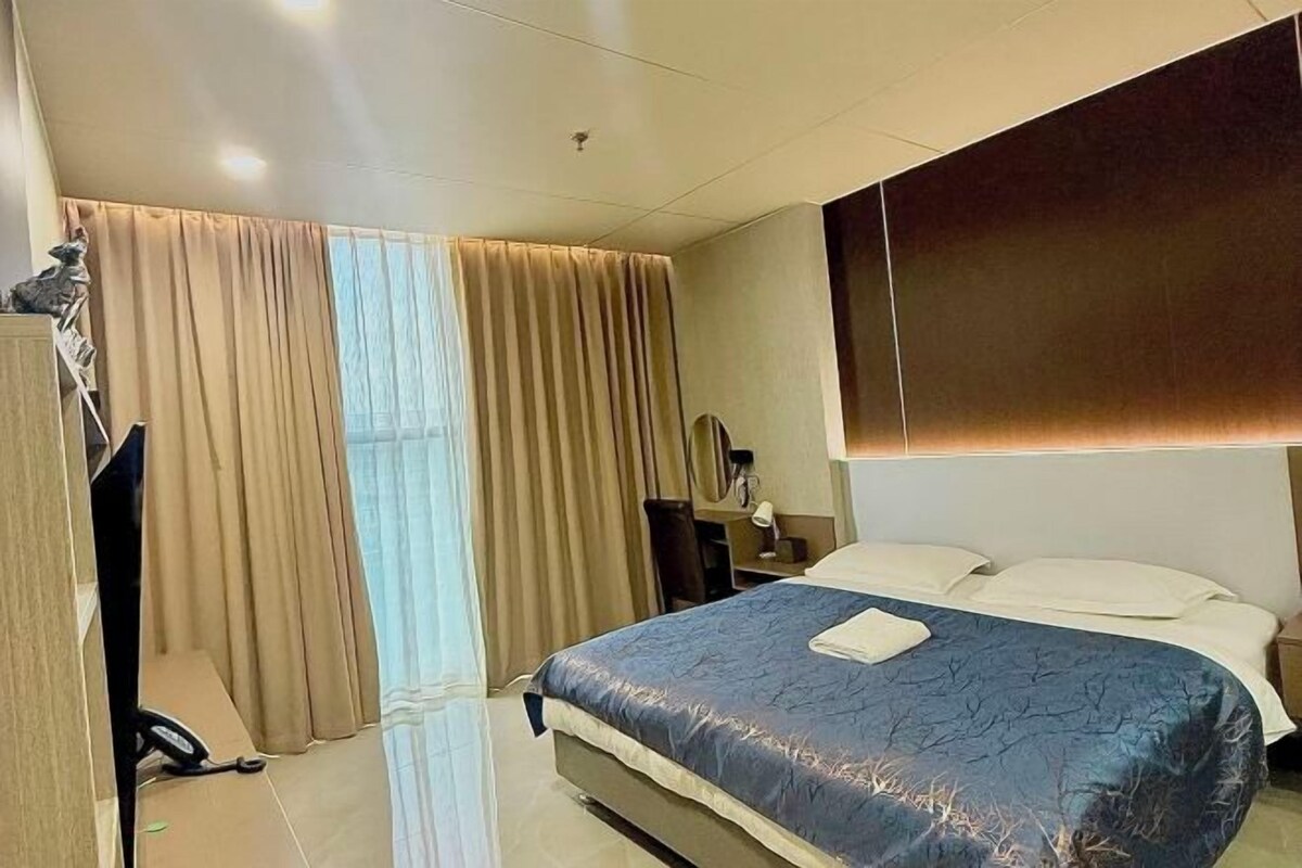 A hotel room with a bed, a desk, a chair, and a wardrobe.