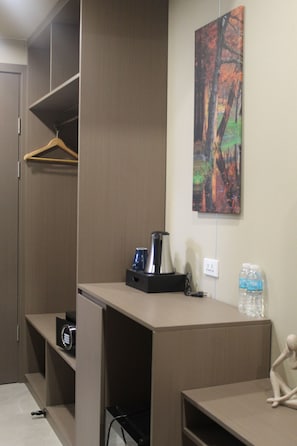 A hotel room with a wardrobe, a desk with a coffee maker, a water bottle, and a painting on the wall. - Skyport Hotel (Pasay)