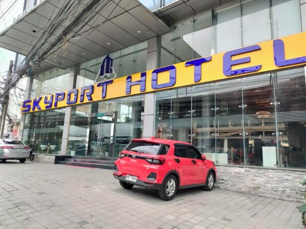 A hotel named "Skyport Hotel" with a modern glass facade and a red car parked in front. - Skyport Hotel (Pasay)