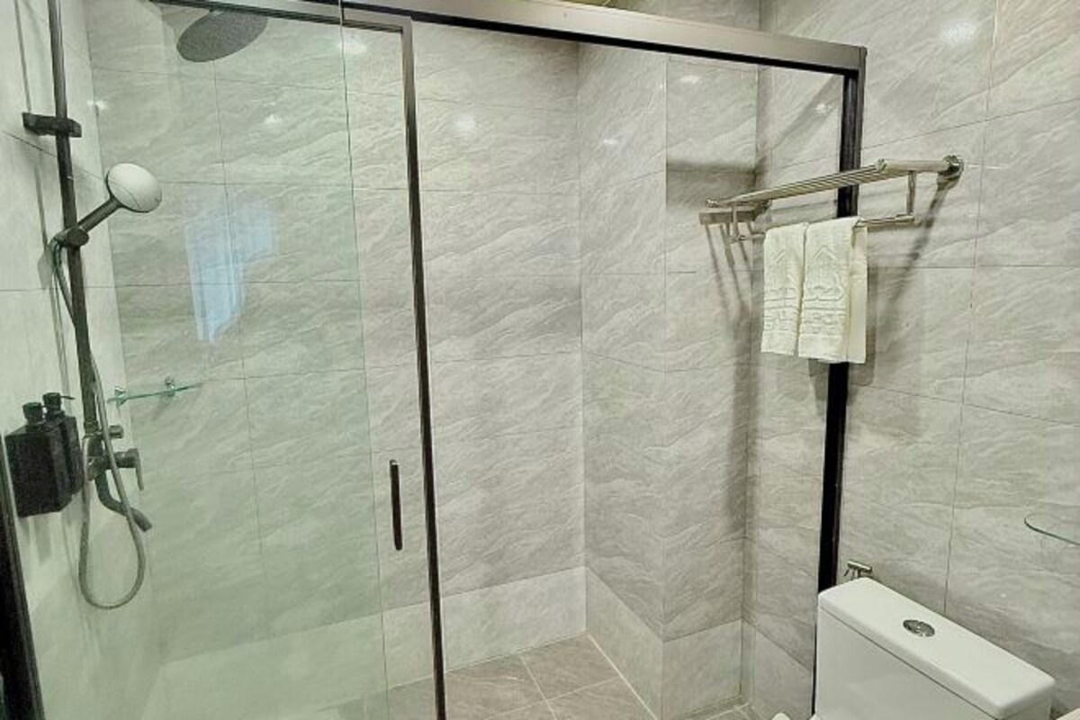 A glass-enclosed shower with a handheld showerhead, a glass door, and a towel rack with a towel.