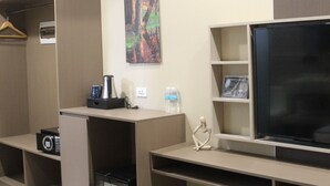 A hotel room with a bed, a desk with a computer, a TV, a small cabinet, a trash can, and an air conditioning unit. - Skyport Hotel (Pasay)