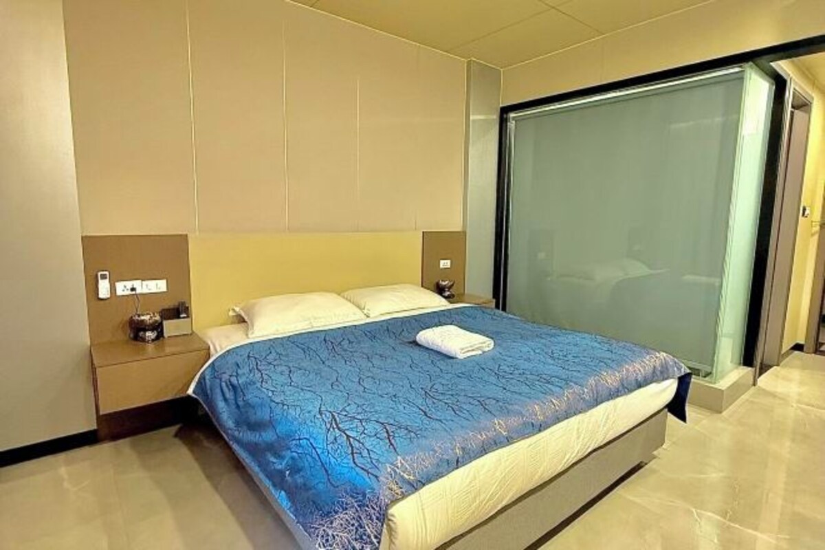 A hotel room with a bed, a nightstand, a wall-mounted lamp, and a sliding door.
