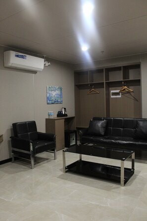 A modern hotel room with a black leather sofa, two armchairs, a coffee table, and a painting on the wall. - Skyport Hotel (Pasay)