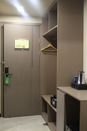 A hotel room with a closed door, a green lock, a hanging coat rack, and a small shelf with a kettle and a cup. - Skyport Hotel (Pasay)