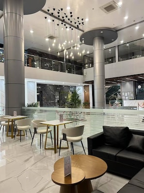 Un espacio interior moderno con una fuente central, zonas de estar y un entrepiso.