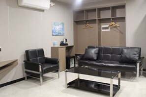 A modern waiting area with a black leather sofa, a black leather armchair, and a glass coffee table. There is a painting on the wall and a coat rack with hangers. - Skyport Hotel (Pasay)