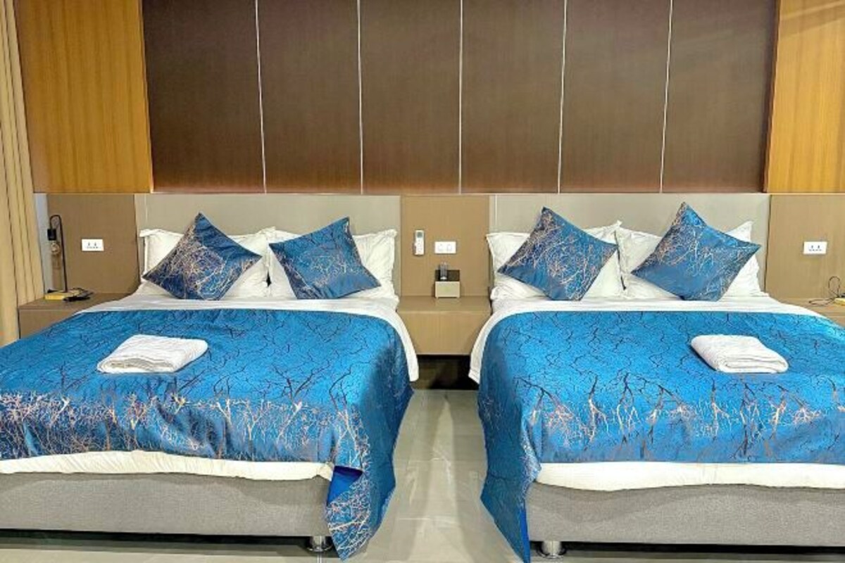 A hotel room with two beds, each with blue bedding and matching pillows.