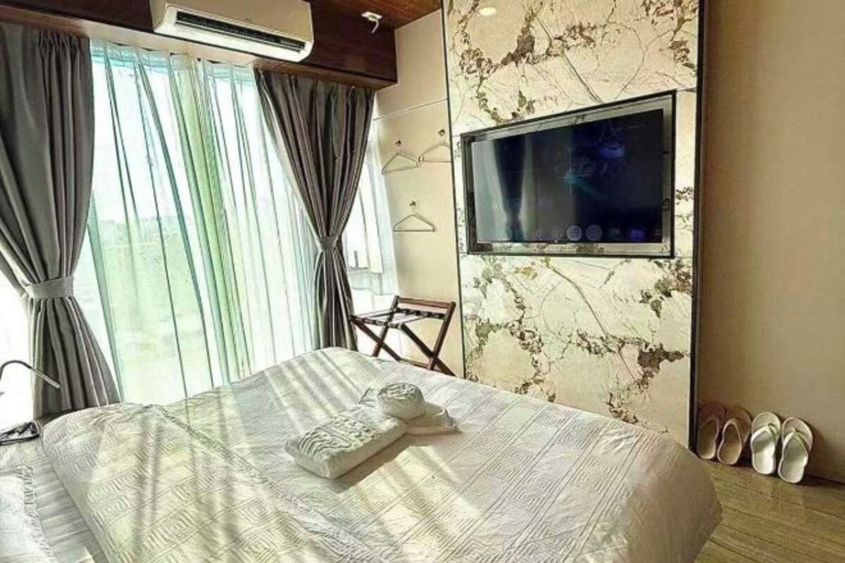 A hotel room with a bed, a TV mounted on the wall, a chair, and a pair of slippers.