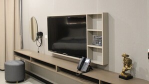 A modern living room with a large flat-screen TV, a small round mirror, a telephone, and a decorative sculpture on a built-in shelf. - Skyport Hotel (Pasay)