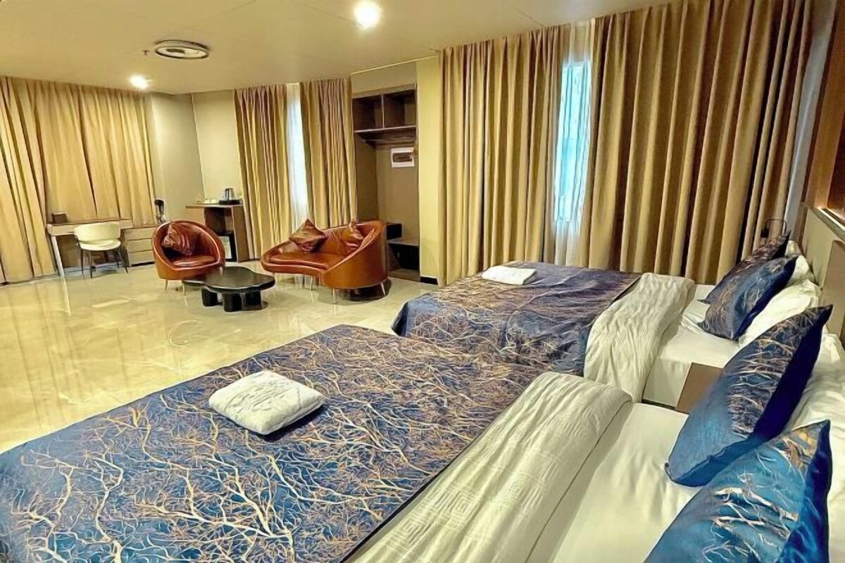 A hotel room with two beds, a sofa, a chair, a desk, and a large window with curtains.