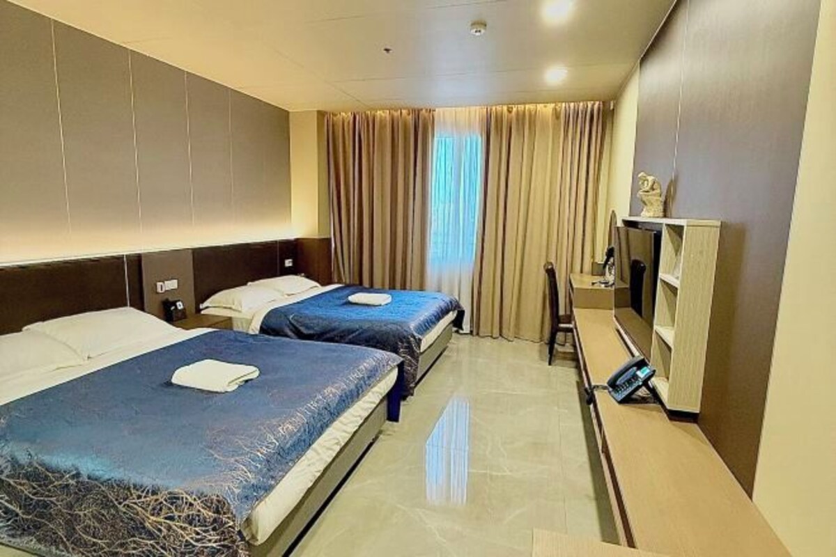 A hotel room with two beds, a TV, a desk, and a window with curtains.