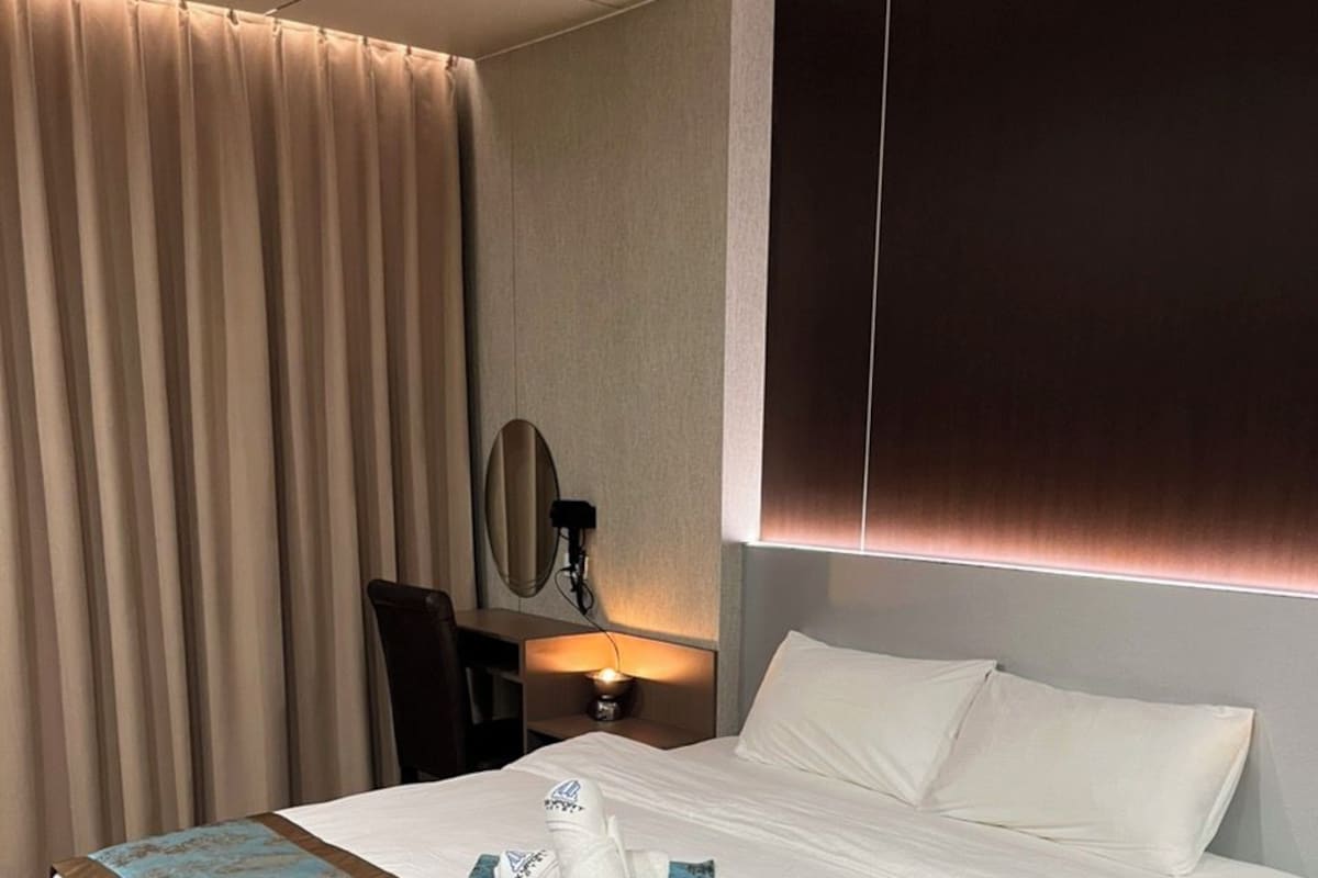 Una habitación de hotel con una cama grande, una mesita de noche con lámpara, un espejo y una cortina.