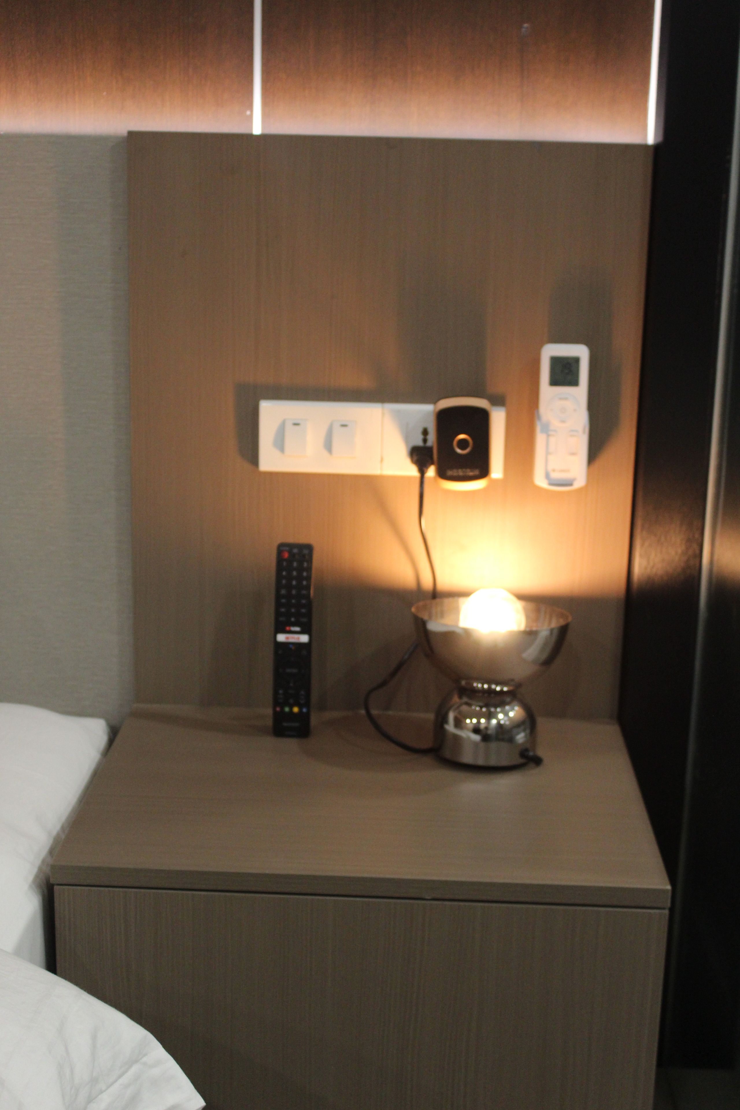 A hotel room with a bedside table, a lamp, a remote control, and a wall-mounted charging station.