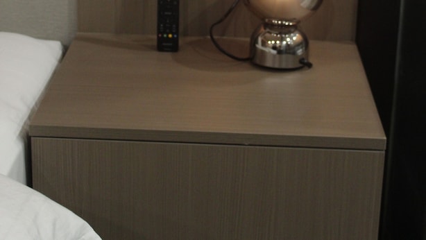 Une chambre d’hôtel équipée d’une table de chevet, d’une lampe, d’une télécommande et d’une station de recharge fixée au mur.