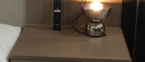 A hotel room with a bedside table, a lamp, a remote control, and a wall-mounted charging station.