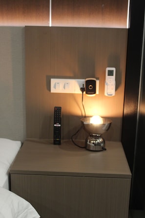 Ett hotellrum med ett nattduksbord, en lampa, en fjärrkontroll och en väggmonterad laddstation.