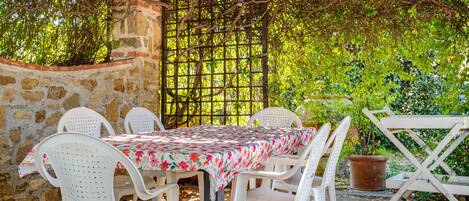 An outdoor patio with a table and chairs, surrounded by stone walls and greenery.