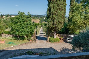 Un chemin pavé mène à une porte, qui est entourée de verdure et à proximité d’un véhicule stationné.
