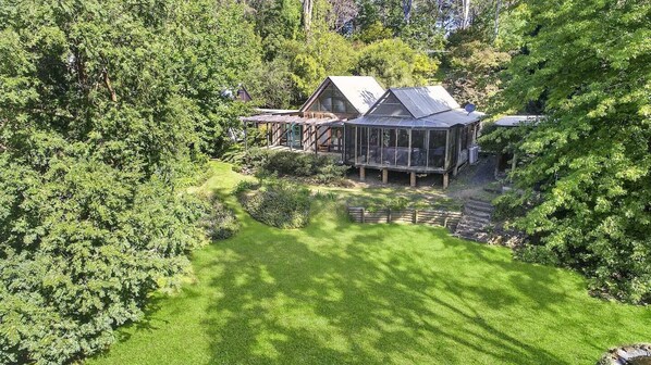 A large house with a glass conservatory, surrounded by lush greenery and a well-maintained lawn. - Peaceful Cabin in National Park (Mountain Lagoon)